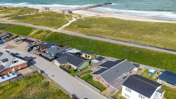 Vue aérienne d’une zone résidentielle côtière, avec des maisons, une plage et une digue rocheuse.