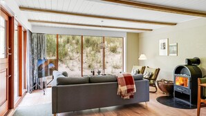Un salon chaleureux avec un canapé, une cheminée et une grande fenêtre donnant sur un paysage naturel.