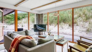 Un salon moderne doté d’un grand téléviseur, de sièges confortables et offrant une vue sur la plage.