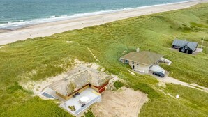 Vue aérienne d’une propriété située sur la côte, avec une plage, des zones herbeuses et une maison dotée d’une terrasse.
