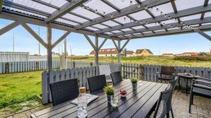 Eine Terrassengruppe im Freien mit Holztisch und -stühlen, einer Pergola darüber und Blick auf Häuser im Hintergrund.