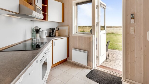 Une cuisine moderne avec des meubles blancs, un four Bosch et une machine à café. Une fenêtre offre une vue sur un champ verdoyant.