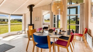 Un vaste espace dédié à la salle à manger, avec une grande table, des chaises aux couleurs vives et un poêle à bois.