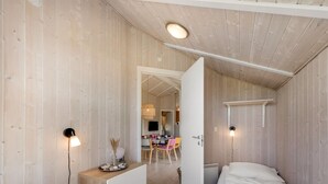 Une chambre avec deux lits, un bureau et une chaise. Une porte donne accès à une autre pièce.