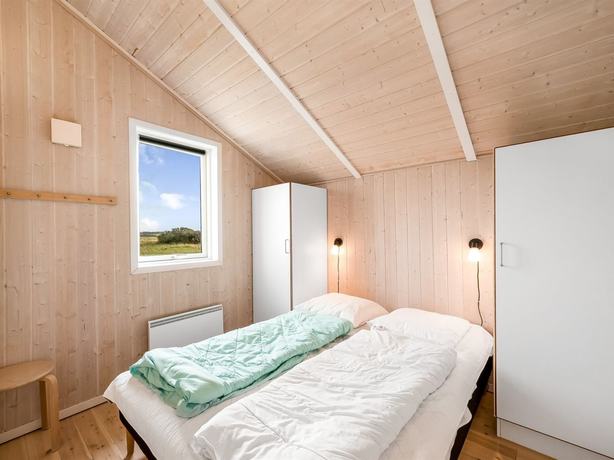 A bedroom with a single bed, a window with a view of the outdoors, and a wardrobe.