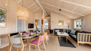 Une pièce spacieuse avec un plafond haut, des murs en bois, un coin repas avec une table ronde et des chaises, un canapé et un téléviseur.