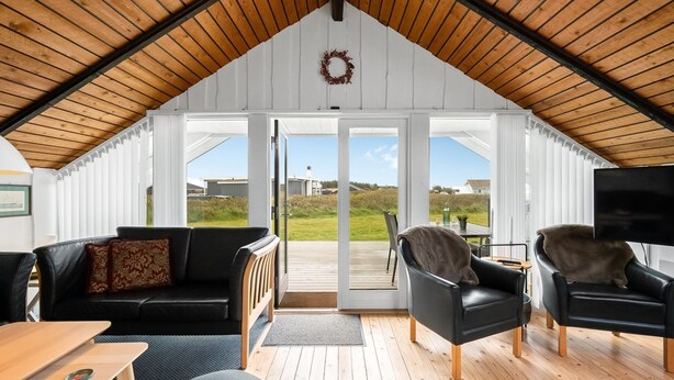 A spacious loft with a high ceiling, a cozy seating area with a sofa and chairs, a flat-screen TV, and a view of the outdoors through large sliding doors. - "Olesia" - 250m from the sea by Interhome (Harboøre)