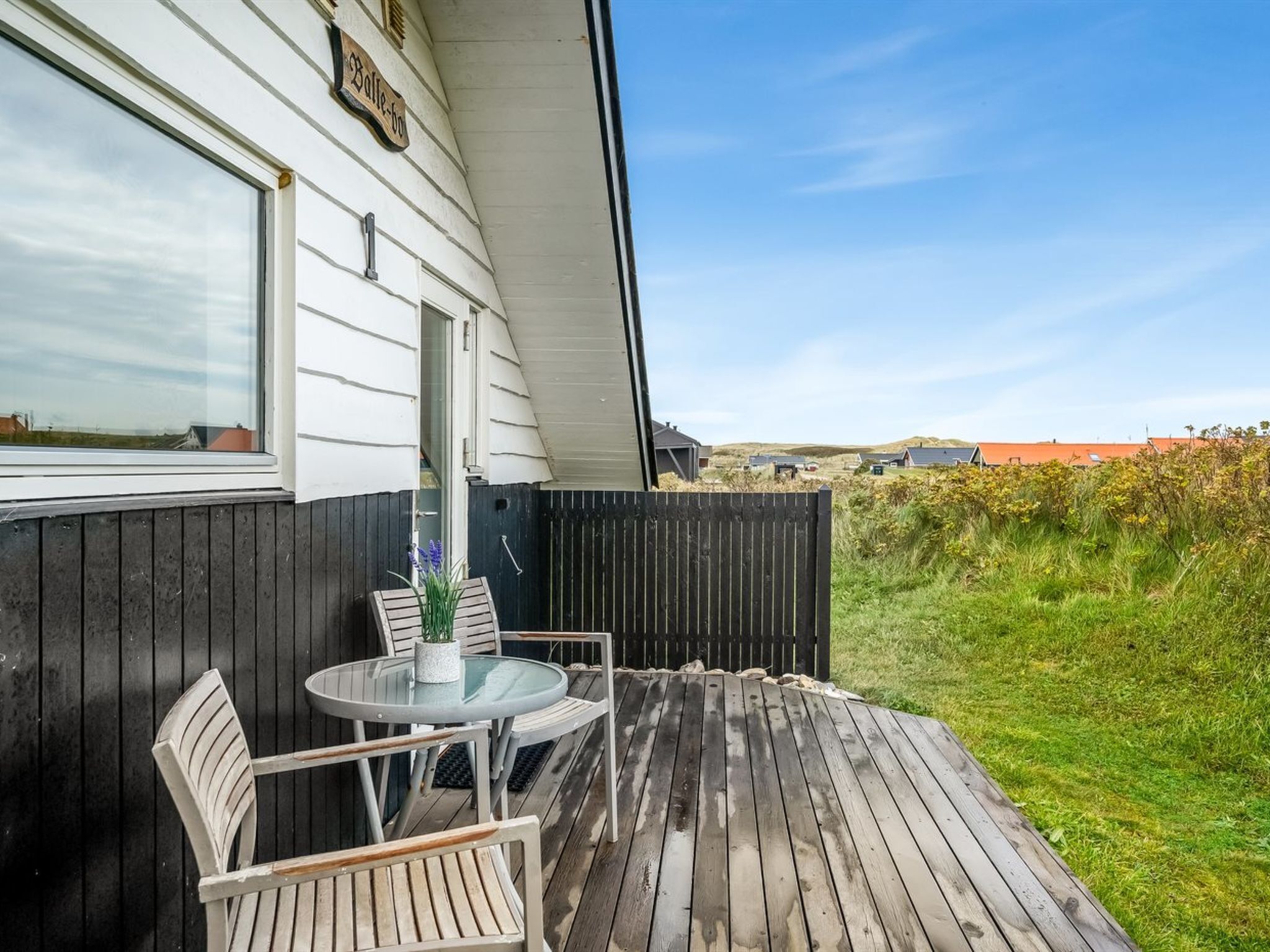 A wooden deck with a table and chairs, a potted plant, and a view of the surrounding landscape.