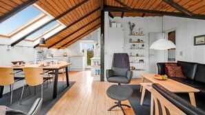 A modern loft with a sloped ceiling, wooden floors, a dining area, a seating area with a sofa and table, and a kitchen visible through an open door. - "Olesia" - 250m from the sea by Interhome (Harboøre)