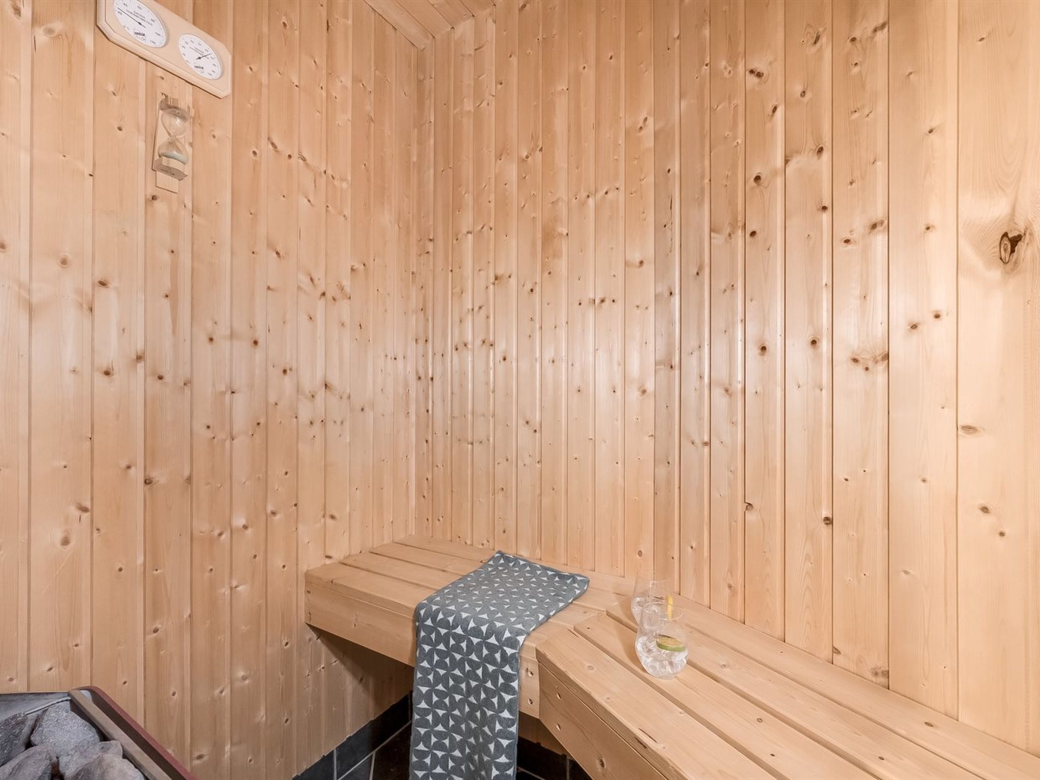 A sauna room with wooden walls, a bench, and a small table with glasses and a bottle.