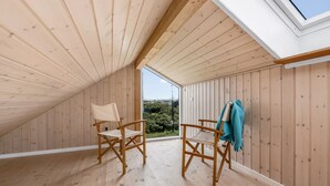 Ein Zimmer im Dachboden aus Holz mit zwei Stühlen, einem Oberlicht und Blick auf Grünflächen.