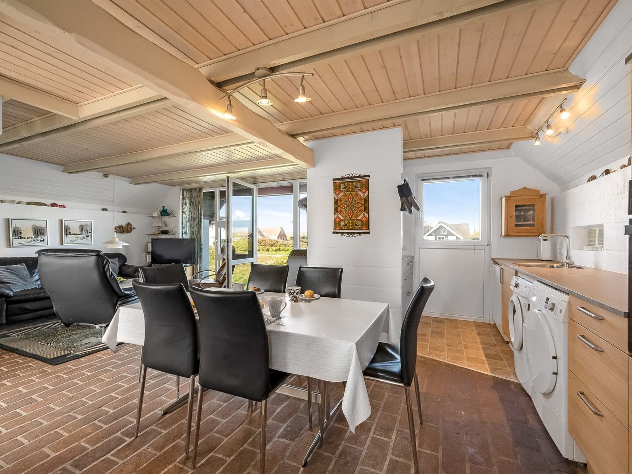 A spacious living area with a dining table, black chairs, and a kitchen with modern appliances.