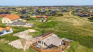 An aerial view of a residential area with houses, a large open grassy field, and a prominent house with a wooden deck and outdoor seating area. - "Arla" - 200m from the sea by Interhome (Harboøre)