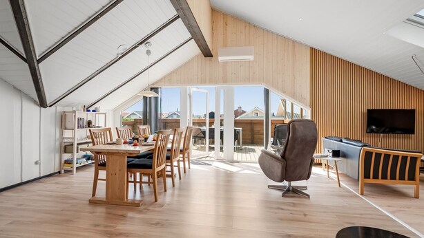 A spacious loft with a high ceiling, wooden flooring, a dining area with a long table and chairs, a seating area with a sofa and armchair, and a television mounted on the wall. - "Arla" - 200m from the sea by Interhome (Harboøre)