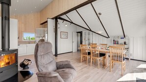 A modern interior with a fireplace, a dining area with wooden chairs, and a kitchen with white cabinets. - "Arla" - 200m from the sea by Interhome (Harboøre)