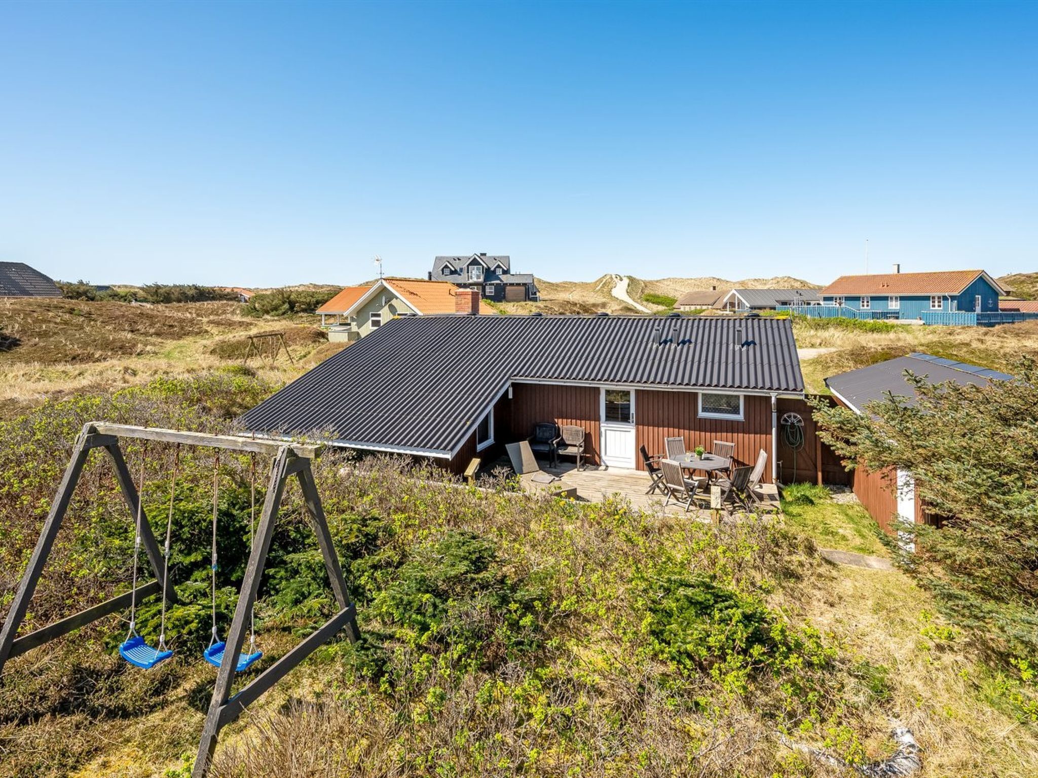 Una casa de techo inclinado, un patio con mobiliario exterior y un columpio en un paisaje natural.