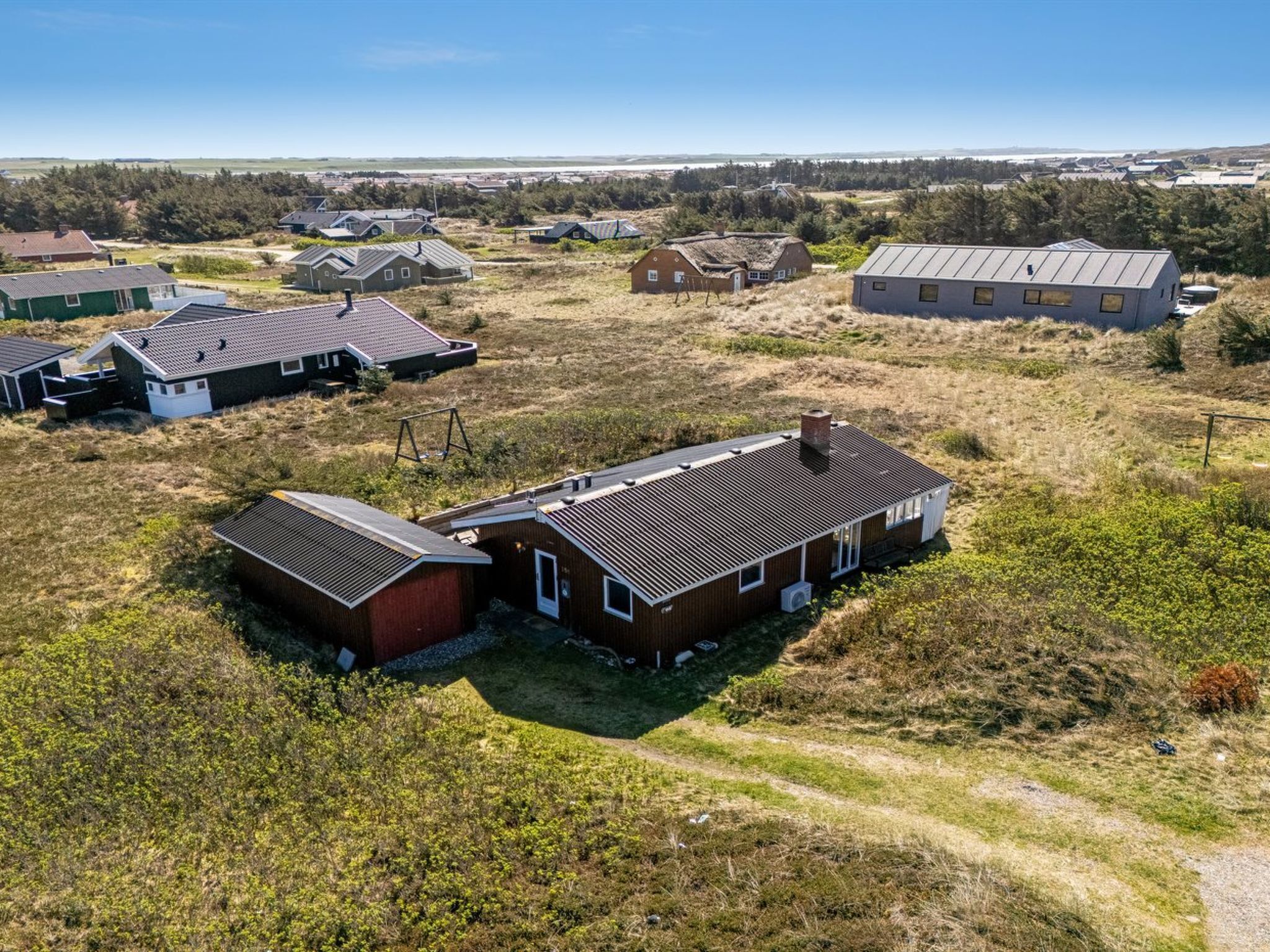 Área residencial com várias casas, algumas com telhados inclinados e outras com telhados planos, cercada por campos gramados e vegetação rala.