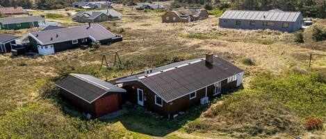 Área residencial com várias casas, algumas com telhados inclinados e outras com telhados planos, cercada por campos gramados e vegetação rala.