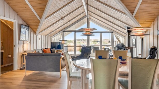 Een ruime kamer met een hoge plafond, een zithoek met stoelen en een tafel, en een groot raam met uitzicht op het landschap.