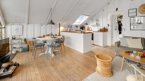 Un loft espacioso con techo alto, zona de comedor con isla central y acogedor rincón de estar con sofá y mesa de centro.