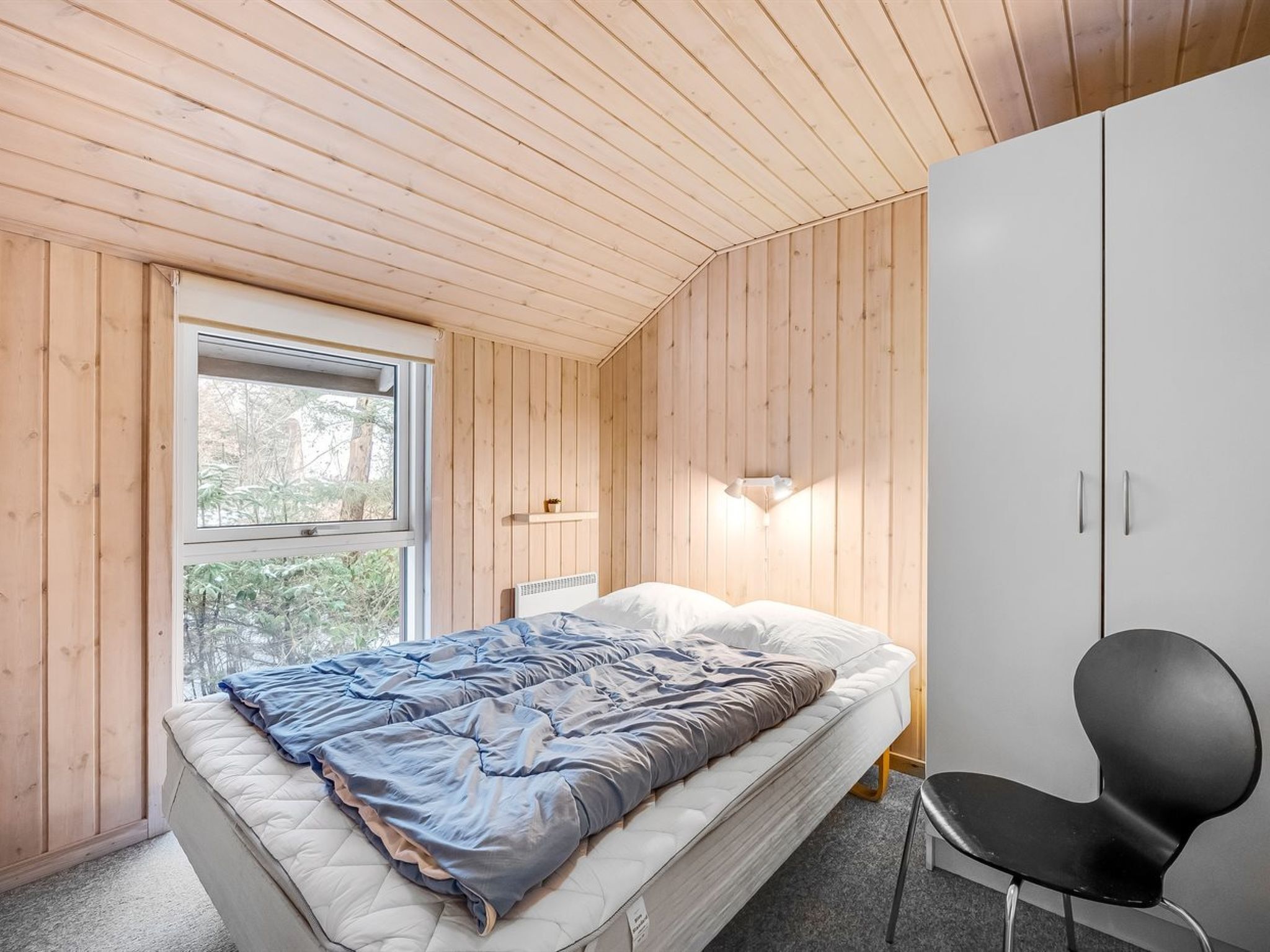 Un dormitorio con cama, una silla, un armario y una ventana.