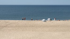 Una playa con gente tomando el sol y caminando por la orilla.