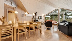 Un interior moderno con una mesa y sillas de madera, un sofá negro y un ventanal con vistas al exterior.