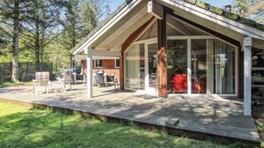 Una casa moderna con una terraza de madera, puerta de entrada de vidrio y un patio con mobiliario exterior.