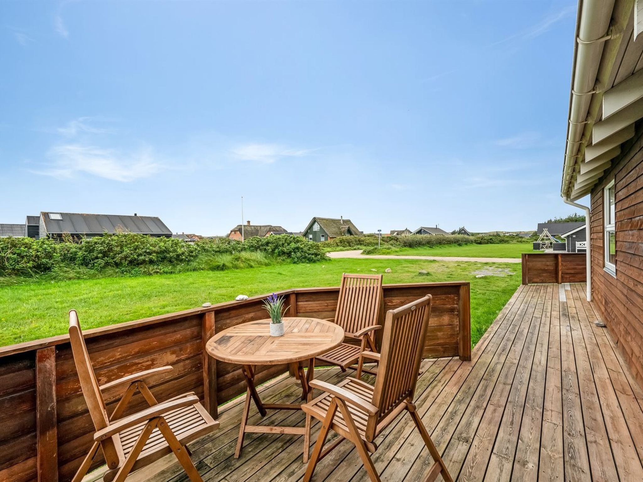 Eine Holzterrasse mit rundem Tisch und Stühlen, mit Blick auf eine Rasenfläche und Häuser im Hintergrund.