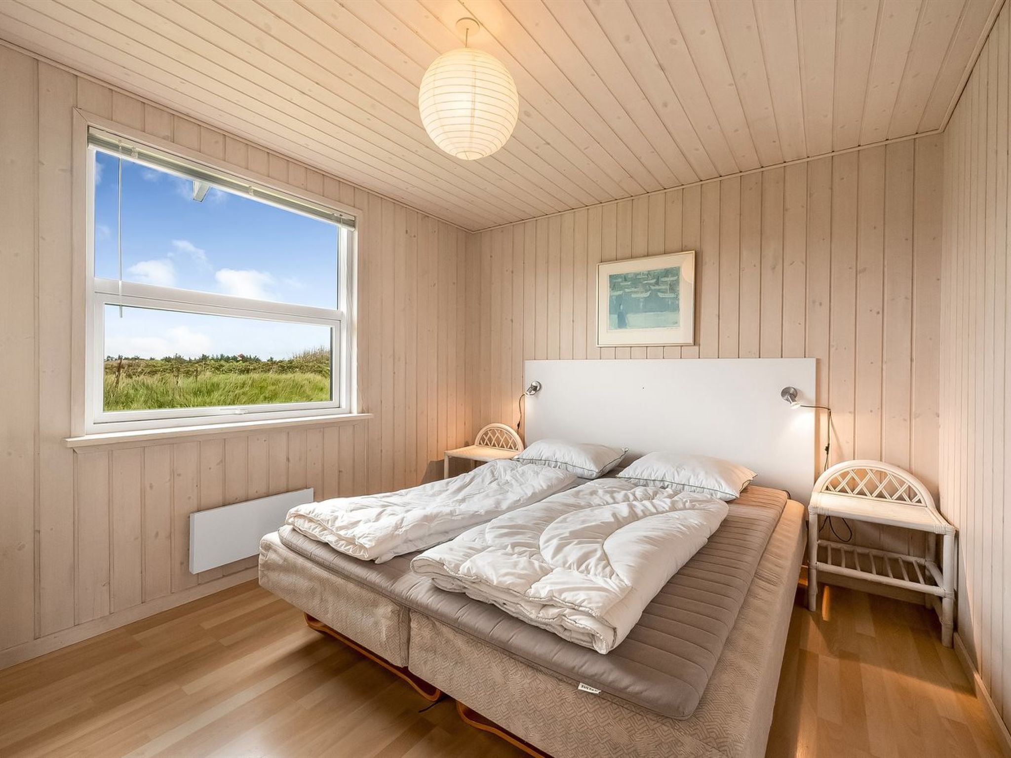 Ein Schlafzimmer mit großem Fenster, einem Bett mit weißer Bettwäsche, einem Kopfteil und einem Nachttisch.