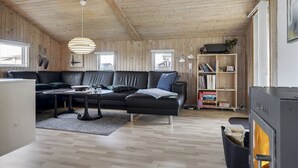 A cozy cabin interior with a wooden ceiling, a black leather sofa, a dining table, and a bookshelf. - "Hebba" - 300m from the sea by Interhome (Harboøre)