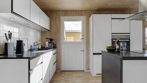 A modern kitchen with white cabinetry, a wooden ceiling, and a view through a door to the outside. - "Hebba" - 300m from the sea by Interhome (Harboøre)