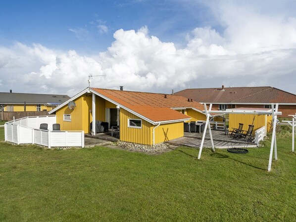 En gul bygning med rødt tag, hvid stakit og et overdækket udendørs siddeområde.