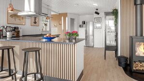 A modern kitchen with a central island, bar stools, a wood-burning stove, and a dining area with a view.