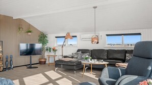 A modern living room with a flat-screen TV, leather sofa, and a large window.