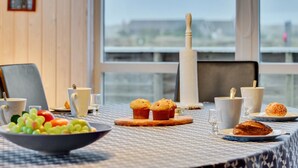 A breakfast setting with a table set for two, including a bowl of fruit, muffins, and pastries.