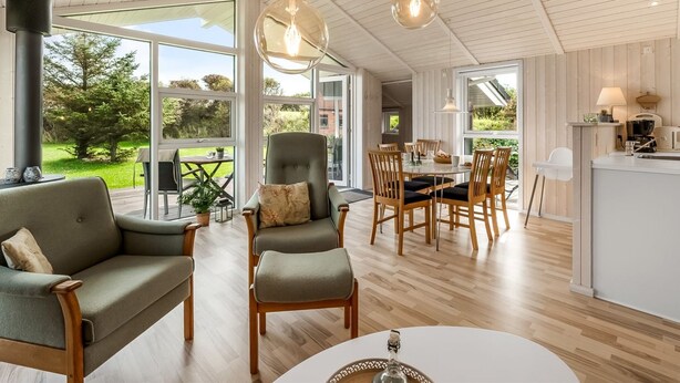 A spacious living area with a dining table, comfortable seating, and large windows offering a view of the outdoors. - "Tanna" - 330m to the fjord by Interhome (Lemvig)
