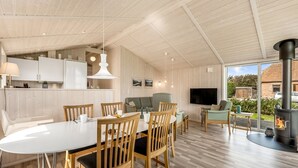 A modern kitchen with white cabinets, a dining area with wooden chairs, and a large TV. - "Tanna" - 330m to the fjord by Interhome (Lemvig)