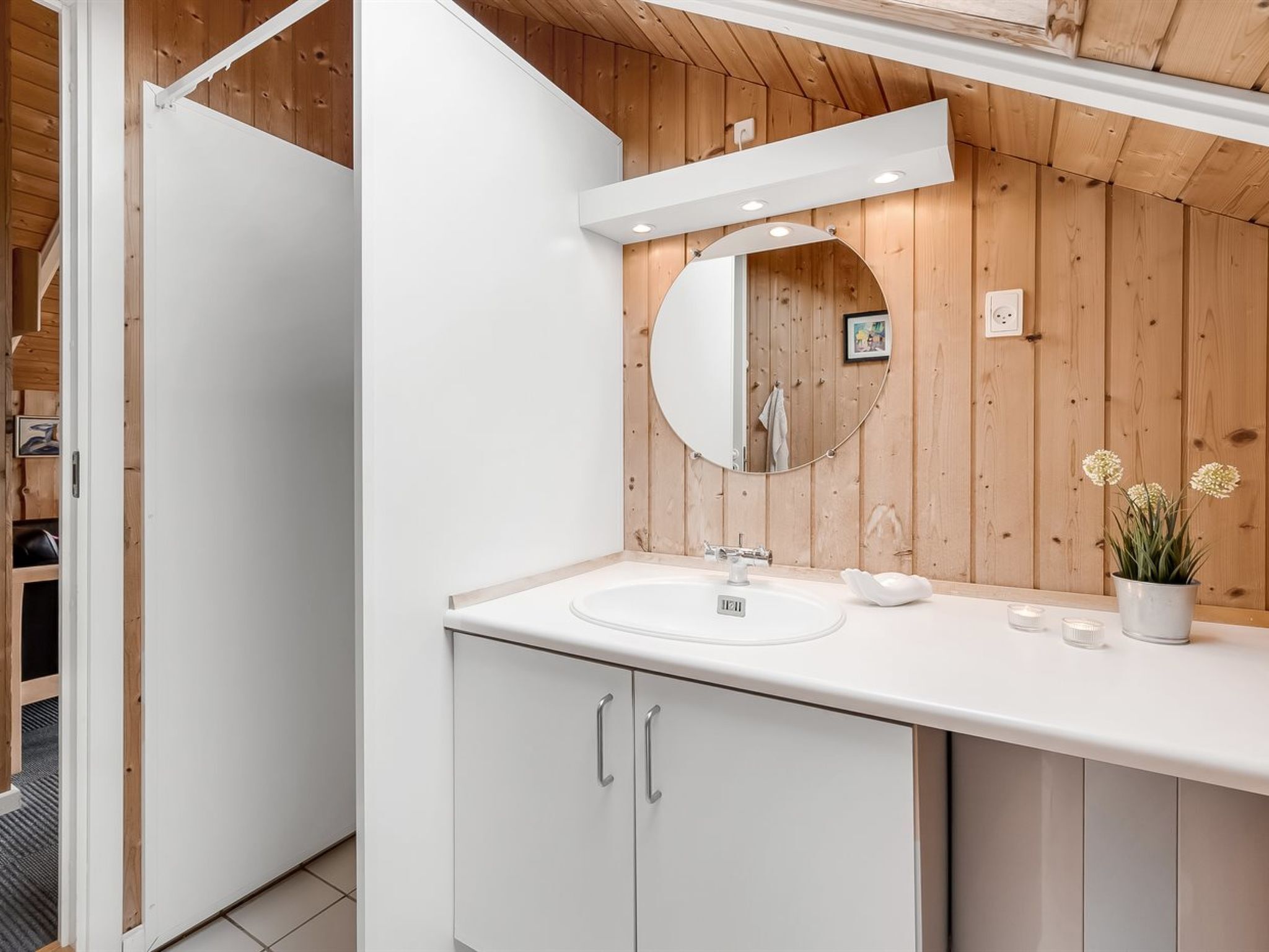 Une salle de bain moderne avec un lavabo blanc, un miroir rond et un lambris en bois sur les murs.