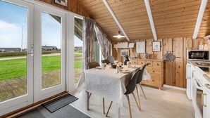 Een gezellig interieur van een blokhut met een eethoek, keuken en grote schuifpuien met uitzicht op een grasveld.