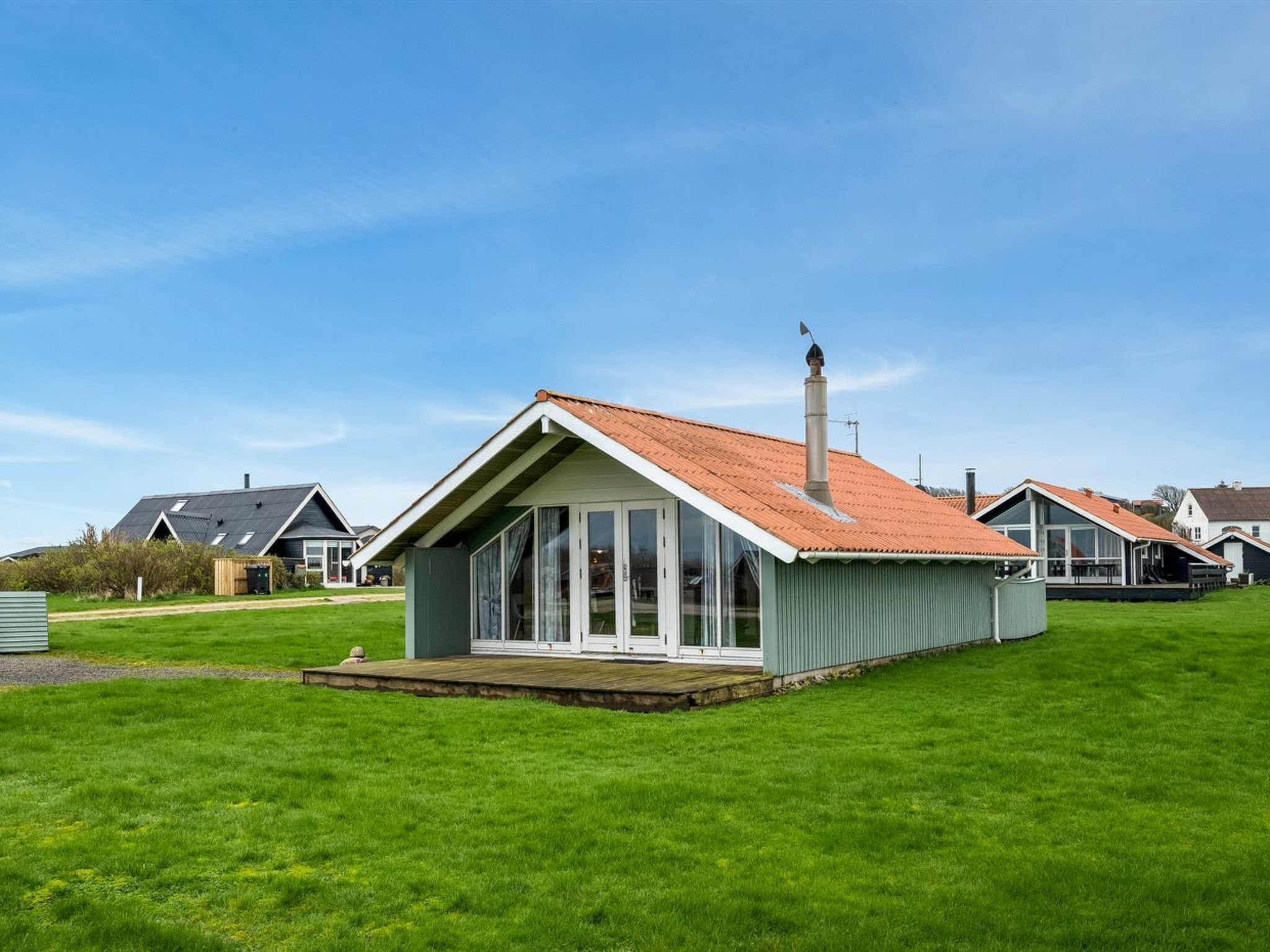 Ein kleines, eingeschossiges Haus mit schrägem Dach und Schornstein, umgeben von einer grünen Rasenfläche und weiteren ähnlichen Häusern im Hintergrund.
