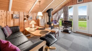 Een knus interieur van een chalet met een houten plafond, een bank, een tafel met een lamp, een televisie en een open haard.