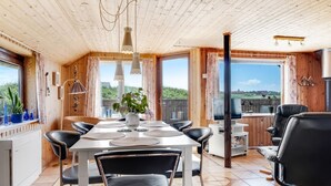 A spacious dining area with a long table and multiple chairs, a kitchen area with a stove and counter, and large windows offering a view of the outdoors. - "Beatrice" - 150m from the sea by Interhome (Lemvig)