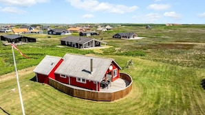 A red house with a wooden deck, surrounded by a grassy field and other houses in the background. - "Beatrice" - 150m from the sea by Interhome (Lemvig)