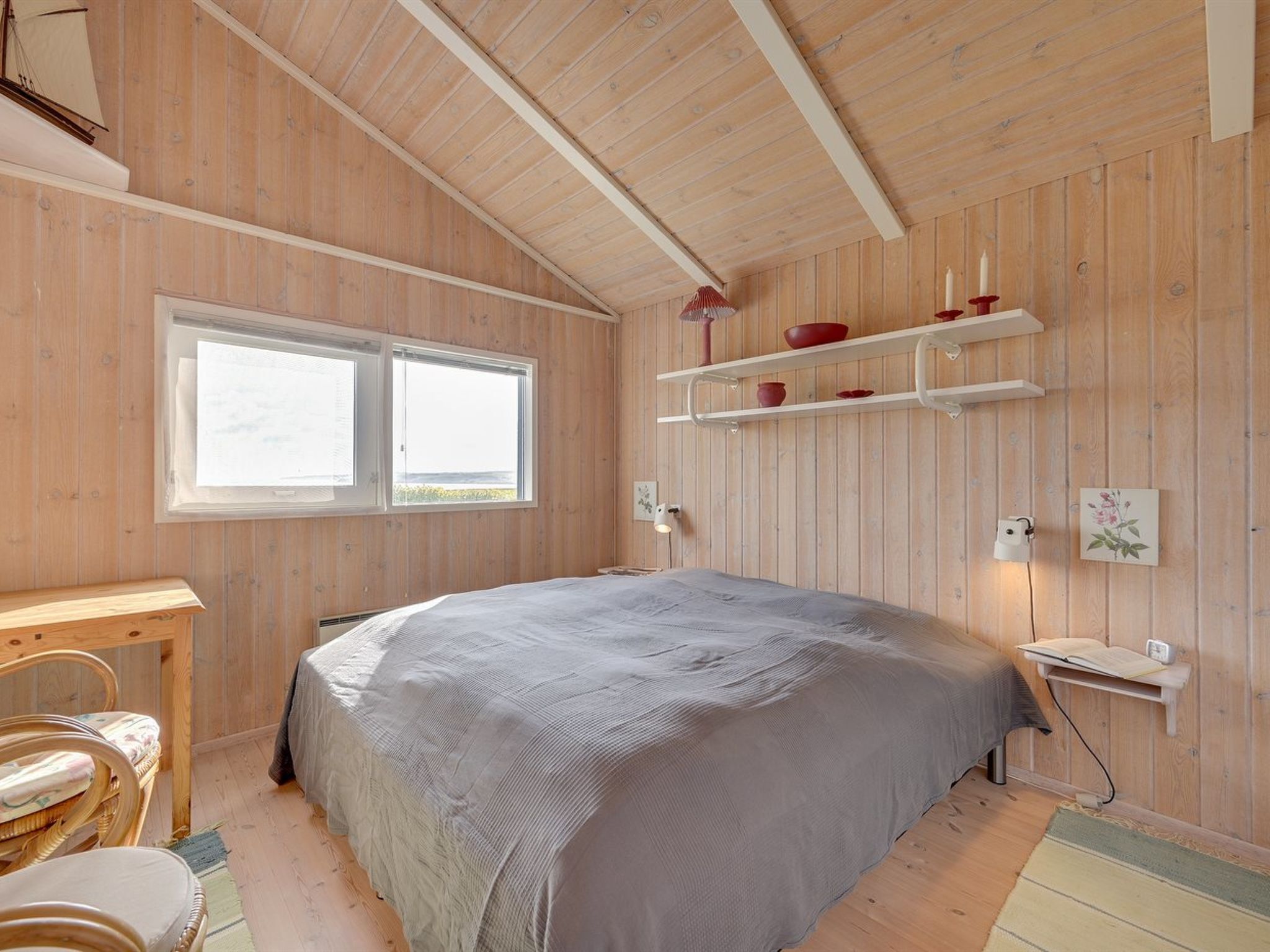 Une chambre aux murs lambrissés, avec un grand lit, un bureau et une fenêtre.