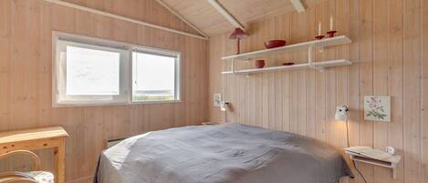 Une chambre aux murs lambrissés, avec un grand lit, un bureau et une fenêtre.