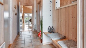 Un pasillo interior de madera con un banco, una lámpara colgante y vistas a otra habitación.
