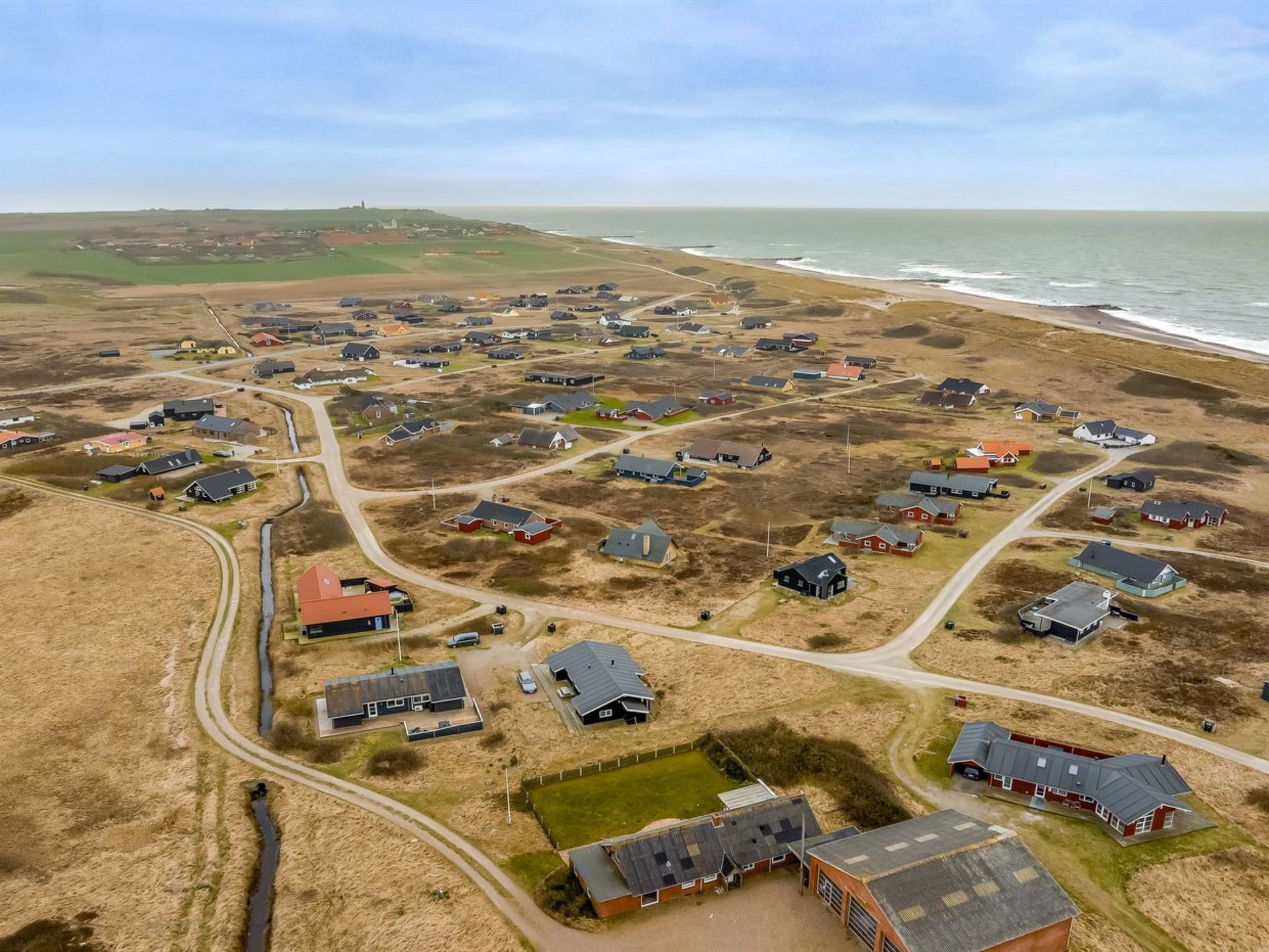 Vue aérienne d’une zone résidentielle côtière, avec des maisons, des routes et une plage.