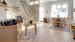 Uma sala de estar moderna com escada de madeira, um sofá, uma mesa de jantar e uma estante.