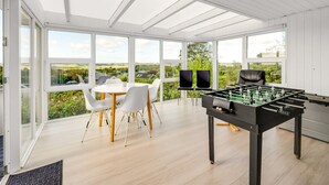 Ein heller, offener Raum mit einem Kicker, einem Esstisch mit Stühlen und großen Fenstern mit Blick auf die Landschaft.